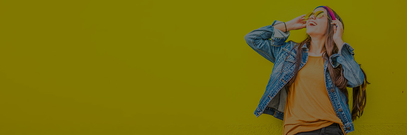 Immagine di una ragazza con cappello e occhiali da soli davanti ad un muro giallo.